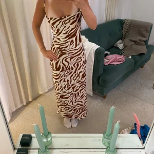 Zebramönstrad långklänning med snörning - Supersnygg långklänning med zebramönster i brunt och vitt. Klänningen har tunna axelband som korsas i ryggen och snörning baktill för en öppen rygg-look. Sval och flowy passform, perfekt för varma dagar🦓