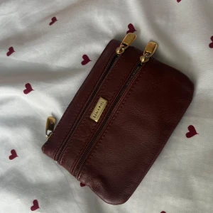 Brun plånbok i äkta skinn från San Pie - Snygg brun plånbok från San Piel i äkta skinn med två dragkedjor i guld och stilren design. Perfekt storlek för kort och mynt, enkel att ha med sig i väskan eller fickan. Klassisk look som passar till allt.