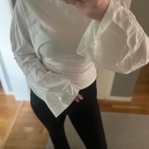 Vit långärmad topp med vida ärmar - Säljer en vit långärmad topp med vida ärmar som ger en cool och trendig look. Toppen är figurnära och har en enkel, stilren design utan mönster eller detaljer. Perfekt för dig som gillar minimalistisk stil och vill sticka ut med ärmarna.