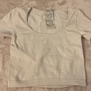 Ribbad vit topp från Amisu - Säljer en ribbad vit topp från Amisu i storlek S. Toppen har korta ärmar, rundad urringning och croppad passform. Perfekt för dig som gillar en enkel men snygg stil. Materialet är mjukt och stretchigt för en bekväm känsla.
