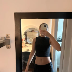 Svart croppad ärmlös topp - Snygg svart croppad topp med hög hals och ärmlös design. Perfekt för att matcha med höga byxor eller kjol. Enkel och stilren look som passar till många outfits.