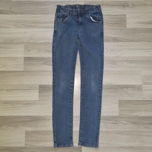 Blå jeansbyxor från Cubus, storlek 164 - Säljer ett par klassiska blå jeansbyxor från Cubus i storlek 164. Byxorna har normal passform, resår i midjan och fem fickor. Snygga kontrastsömmar och en enkel, tidlös look som funkar till det mesta. Perfekta för dig som gillar bekväma och stilrena jeans.