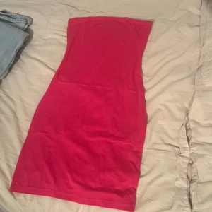 Mörk rosa axelbandslös kortklänning - Snygg mörk rosa axelbandslös kortklänning med figurnära passform. Klänningen är enkel och stilren utan mönster eller detaljer, perfekt för dig som gillar en clean look. Tillverkad i mjukt material som känns skönt mot huden.