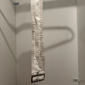 Brett vitt jeansbälte - Säljer ett brett vitt bälte i jeansmaterial med dubbla rader av metallöljetter och ett fyrkantigt metallspänne. Perfekt för att lyfta din outfit! 🤍