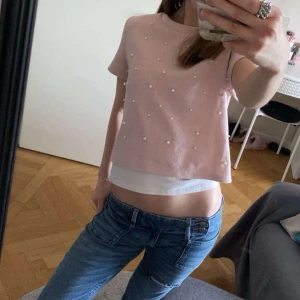 Rosa pärlprydd topp från H&M Divided - Supersöt ljusrosa topp från H&M Divided med korta ärmar och rund hals. Toppen är dekorerad med små pärlor över hela framsidan för en extra söt vibe. Modellen är croppad och har en avslappnad passform, perfekt till jeans eller kjol. Tröjan är i storlek Xs men passar även S.