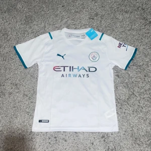 Manchester City vit bortatröja Puma limiter edition - Snygg limited edition Manchester City bortatröja från Puma i vitt med turkosa detaljer på ärmslut och axlar. Broderad klubbmärke på bröstet, Puma-logga och Etihad Airways-tryck framtill. Helt ny och aldrig använd