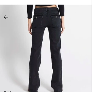 Svarta bootcut jeans med fickdetaljer - Snygga svarta jeans med bootcut passform och coola fickor med lock och knappar bak. Jeansen har låg midja och klassisk femficksdesign. Perfekta för dig som gillar en avslappnad men ändå trendig look. I storlek xxs