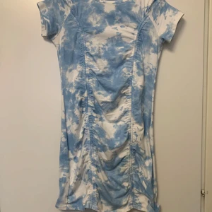 Blåvit kortklänning med rynk - Superfin kortklänning i blått och vitt med tie-dye mönster. Klänningen har korta ärmar och snygga rynkade detaljer framtill som ger en cool och trendig look. Perfekt för dig som gillar en avslappnad men ändå stylish stil.