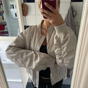 Beige bomberjacka med dragkedja Stockh LM - Snygg beige bomberjacka med klassisk ribbad krage och muddar. Stockh lm, storlek xs