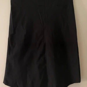 Svart långkjol med kardborreknäppning - Enkel svart kjol med rak passform och bred midja som stängs med kardborre. Kjolen är stilren och passar perfekt till en clean look. Materialet känns som bomull eller polyester och kjolen är helt utan mönster eller detaljer.