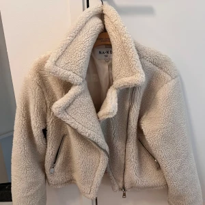 Beige teddyjacka från NA-KD - Säljer en supermjuk och fluffig teddyjacka från NA-KD i beige. Jackan har bred krage, dragkedjor i silver på fickor framtill. 