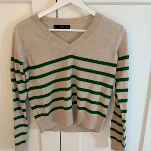 Beige randig tröja från mango - Beige stickad tröja från mango med gröna horisontella ränder. V-ringad halsringning och långärmad modell. Perfekt för dig som gillar en klassisk men ändå chill stil. Skön passform och enkel att matcha med jeans eller kjol.