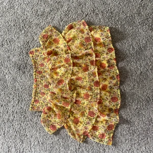 Gul blommig volangkjol från Lindex - Supersöt kort kjol från Lindex i gul färg med blommigt mönster i rött och grönt. Kjolen har flera volanger och smock i midjan för en bekväm passform. Perfekt för dig som gillar färgglada och lekfulla plagg!❤️