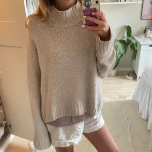Beige stickad polotröja - Mysig beige stickad polotröja med oversized passform och långa ärmar. Tröjan har en hög, ribbad krage och breda muddar vid ärmslut och nederkant. Perfekt för lager-på-lager och chill höst- eller vinterdagar.