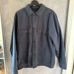 Mörkblå overshirt med fickor - Snygg mörkblå overshirt med klassisk krage och två stora bröstfickor med knappar. Jackan har raka linjer, knäppning framtill och långa ärmar. Perfekt att slänga över en hoodie eller t-shirt för en chill look.