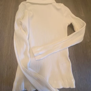 Vit ribbad polotröja från Zara - Vit ribbad polotröja från Zara med lång ärm och tight passform. Tröjan har hög krage och är tillverkad i ett stretchigt material som sitter snyggt. Perfekt att styla med jeans eller kjol för en clean look.