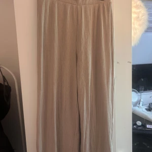 Beige ribbade byxor från XOXO Friends - Snygga ribbade byxor i beige från XOXO Friends. Byxorna har en rak och loose passform med hög midja och breda ben. Tillverkade i mjukt material som känns skönt mot huden. Perfekta för en chill och avslappnad look.