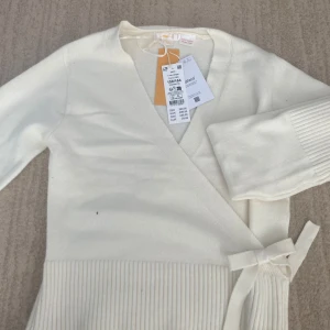 Krämvit omlottkofta från Gina Tricot - Superfin krämvit omlottkofta från Gina Tricot med knytband i sidan och bred ribbad kant nedtill. Koftan har lång ärm och är stickad i mjukt material, perfekt för lager på lager. Enkel och stilren design som passar till allt.