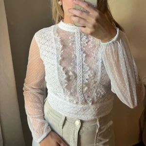 Vit spetsblus - Superfin vit blus i spets och mesh. Blusen har spetsdetaljer framtill och en öppen rygg med bred knytrosett bak💕
