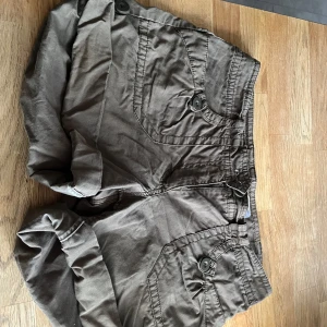 Armégröna shorts med fickor från H&M - Snygga armegröna shorts från H&M med stora fickor framtill och baktill, alla med knappdetaljer. Modellen har midwaist passform och är tillverkad i mjuk bomull. Perfekta för sommardagar när du vill ha en avslappnad och cool stil.