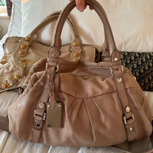 Ljusrosa beige väska med emblem - Köp helst via min vinted för bättre pris @juliavallberg 🤍Så fin ljusrosa beige handväska med silverdetaljer. Använt skick men fullt funktionell. Supersnygg unik väska med ett tjockare kortare axelband och dubbla handtag. Liknande modellen Q Classic Baby Groove! Kan skickas eller hämtas hos mig i Nacka 🤍