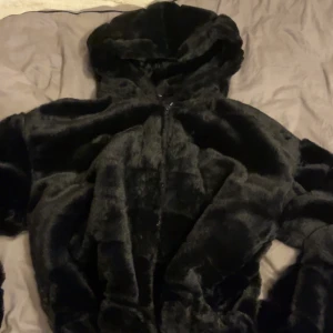 Svart pälsjacka - Mysig svart pälsjacka med huva och dragkedja framtill. Jackan har en fluffig känsla och är perfekt för kalla dagar. Snygg och enkel att matcha med olika outfits, passar dig som gillar en trendig och varm look. Jackan köptes i USA för cirka 3000kr, den är i bra skick 