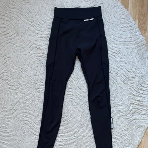 Svarta träningsbyxor från iami  - Säljer ett par supersköna träningsbyxor från iami, gjorda på PET-flaskor, bred midja, praktiska sidofickor och ventilerat meshtyg längs benen som ger en svalkande känsla och en sportig vibe. Perfekta för träning eller chill, med stretchigt syntetmaterial som sitter skönt hela dagen.