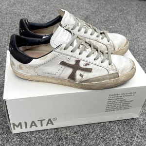 Vita sneakers från Premiata - Snygga vita sneakers från Premiata med grå snörning och svart häl. Nypris 2700 kr. Okej, skick, slitna i hälen. Pris kan diskuteras!