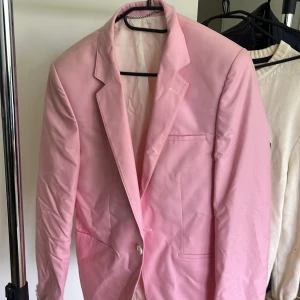 Rosa kavaj från Adrian Hammond - Limited Edition rosa kavaj från Adrian Hammond. Klassisk modell med smala slag, två framfickor och en bröstficka. Snyggt helfodrad och perfekt för dig som vill sticka ut med en färgstark look.