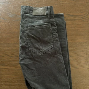 Tiger of Sweden Jeans Svarta 31/34 - Svarta jeans från Tiger of Sweden i modellen Evolve. Klassisk femficksdesign med snygga detaljer och metallknapp med logga. Jeansen har en rak passform och är tillverkade i bomull med en stilren look. Storlek 31 i bredd 34 i längd. 