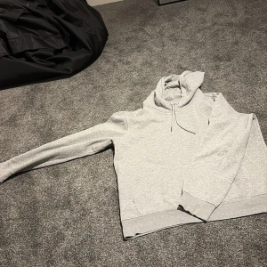 Grå hoodie Mira Paris med tryck - Snygg grå hoodie från Mira Paris med svart tryck på ryggen där det står 'Mi Amor' och ett hjärta med pil. Tröjan har huva med snörning, känguruficka och långa ärmar. Perfekt för chill dagar och streetstyle. 