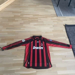 AC Milan långärmad Ronaldo 99 tröja - Säljer en klassisk AC Milan långärmad fotbollströja från Adidas med Ronaldo 99 på ryggen. Tröjan är röd och svart med vertikala ränder, Champions League-märke på ärmen och Bwin som sponsor på bröstet. Broderat klubbmärke och guldiga detaljer. Perfekt för samlare eller fans. Pris går att diskutera.