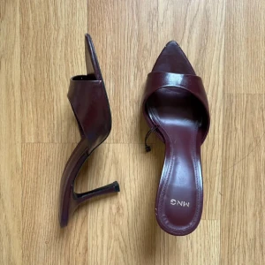 Vinröda klackpumps från Mango - Snygga vinröda pumps från Mango med spetsig tå och hög klack. Skorna är i glansigt skinn och har en öppen design framtill. Perfekta för att lyfta din outfit med en elegant touch.