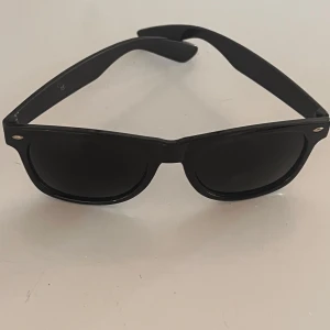Svarta klassiska solglasögon - Snygga svarta solglasögon med tidlös wayfarer-inspirerad form. Bågarna är helsvarta och har små silvriga detaljer vid hörnen. Perfekta för att ge en cool vibe till din outfit. Lätta och bekväma att bära hela dagen.