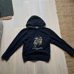 Svart hoodie från U.S. Polo Assn XS - Svart hoodie från U.S. Polo Assn i storlek XS med broderad polospelare på bröstet och vit logga. Klassisk huva med snörning och ribbade muddar. Mjuk insida och sportig känsla, perfekt för chill dagar. hoodien är i nyskick och har inga defekter eller annat, så hör av dig ifall du har tankar eller funderingar 👍