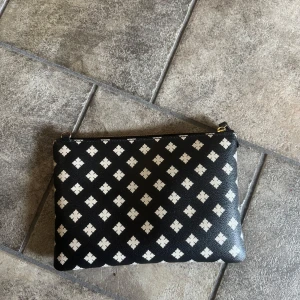 Malene Birger clutch  - Snygg svart Malene Birger clutch med vitt rutmönster och guldfärgad dragkedja. Väskan är i perfekt skick då den ej använts så mycket och det finns inga defekter.