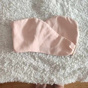 Ljusrosa axelbandslös tubtopp  - Snygg ljusrosa tubtopp med asymmetrisk skärning och axelbandslös design. Toppen har en stilren look och stängs med dragkedja i sidan. Perfekt för att skapa en trendig och chic outfit från nakd. .