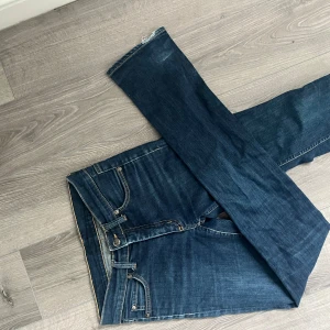 Acne Action Jeans raka blå jeans - Säljer ett par klassiska Acne Action Jeans i mörkblå denim. Jeansen har raka ben, fem fickor och snygga kontrastsömmar. Märkespatch i mocka baktill. Perfekta för dig som gillar stilrena och tidlösa jeans.
