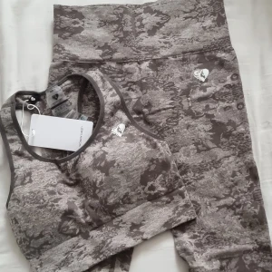 Camo seamless sport-bh från Women's Best - Sportig seamless camo-bh från Women's Best i grågrön camouflage. Bh:n har bred resår under bysten och brottarrygg för extra stöd. Perfekt för träning och har en cool, modern look. Materialet är stretchigt och följsamt för maximal komfort.