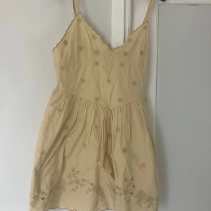 Beige broderad kortklänning från Zara - Supersöt beige kortklänning från Zara med tunna axelband och broderade blommor. Klänningen har v-ringning, dragkedja i sidan och vågig kant nertill. Perfekt för varma dagar. Skick 10/10. 