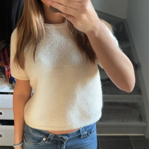 Vit stickad kortärmad tröja - Supermjuk och fluffig vit stickad tröja med korta ärmar och rund hals. Modellen är lite croppad och passar perfekt till jeans eller kjol. Enkel och stilren design som är lätt att matcha med andra plagg.