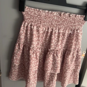 Rosa blommig volangkjol med smock - Supersöt kort kjol i ljusrosa med små vita blommor och volanger. Storlek S