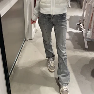 Grå bootcut jeans med fickor - Säljer ett par grå jeans med bootcut-modell och markerade sömmar. Byxorna har stora fickor framtill och en snygg, lite utsvängd passform. Perfekta för dig som gillar en avslappnad men trendig stil.