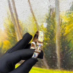 Herms armband med färgglada detaljer - Superfint armband från Herms i guldtonad metall med vit bas och färgglada mönster. Armbandet har den ikoniska H-spännet och är dekorerat med små motiv i rosa, blått, grönt och gult. Perfekt statement piece för dig som gillar lyxiga accessoarer.