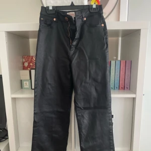 Svarta raka jeans med glansig finish - Snygga svarta jeans med glansig finish och raka ben. Klassisk femficksmodell med knapp och dragkedja framtill. Passar perfekt till en cool streetstyle-look och är lätta att matcha med det mesta. Är lite tajtare vid magen än vid låren. 