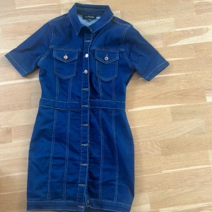 Mörkblå jeansklänning från Parisian - Snygg mörkblå jeansklänning från Parisian med kort ärm, knappar framtill och två bröstfickor. Klänningen har markerad midja och klassisk skjortkrage, perfekt för en cool och avslappnad look. Obs liten i storleken uppskattningsvis för 36/38