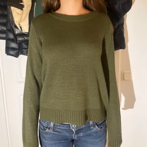 Olivgrön stickad tröja med rund hals - En olivgrön stickad tröja med rund halsringning och långa ärmar. Tröjan har ribbade muddar vid ärmslut och nederkant, vilket ger en snygg och enkel look. Perfekt att slänga på sig till jeans för en chill stil.