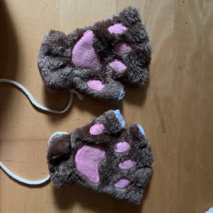 Bruna pälsiga tasshandskar med rosa detaljer - Lite använda och lite smutsiga och original pris var 250kr. Supermjuka och fluffiga handskar som ser ut som djurtassar! De är bruna med rosa trampdynor och öppna fingrar, om du undrar över något eller vill prata om priset kontakta mig! ❤️ 