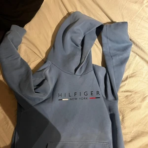Blå hoodie Tommy Hilfiger S - Säljer en blå hoodie från Tommy Hilfiger i storlek S. Tröjan har klassisk huva, magficka och tryckt logga på bröstet med texten 'Hilfiger New York'. Mjuk insida och snygga Hilfiger-detaljer vid halsen. Perfekt för chill dagar.