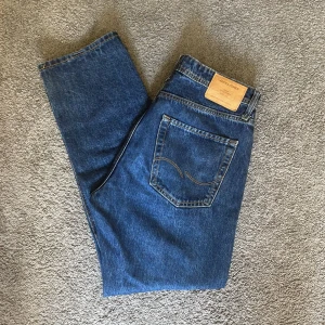 Jack & Jones Relaxed Chris jeans blå 32/32 - Säljer ett par blå jeans från Jack & Jones, modell Relaxed Chris. Klassisk femficksdesign, raka ben och avslappnad passform. Jeansen är i kraftig denim med snygga kontrastsömmar och har en läderpatch bak i midjan.